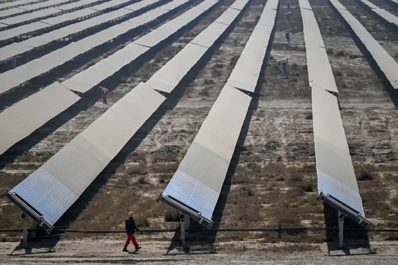 یک کارگر در حال عبور از کنار ردیف‌های پنل‌های خورشیدی در پارک انرژی‌های تجدیدپذیر خوادا.